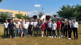 A group of people on a meadow in front of an airplane.