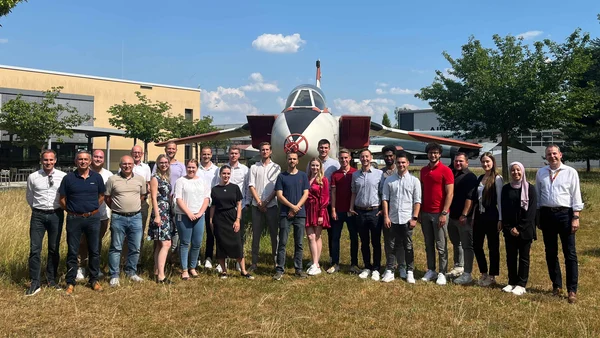 A group of people on a meadow in front of an airplane.