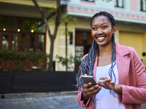 Frau, die auf einer Straße läuft, lacht und ein Smartphone in der Hand hat.