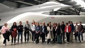 Students in a large factory hall standing in front of aircrafts