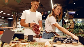 Ein junger Mann und eine junge Frau halten an der Obsttheke Trauben in der Hand