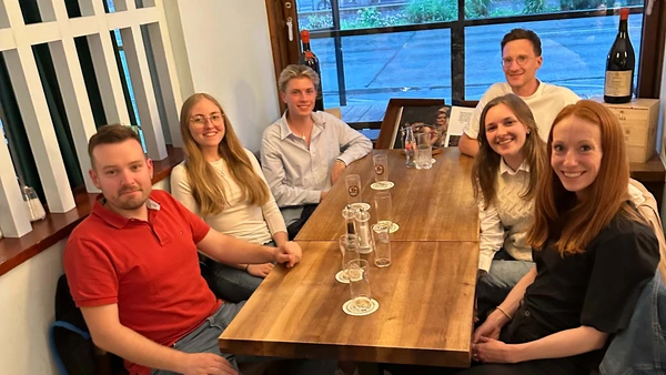 Six people sit around a restaurant table and look into the camera.